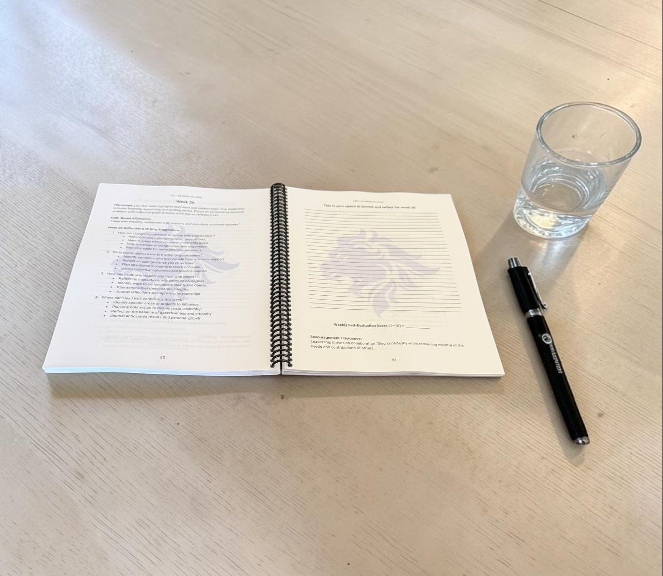 Leo 52-Week Zodiac Journal with a pen and glass of water on a wooden table