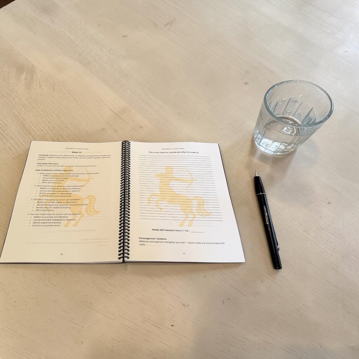 Sagittarius 52-week zodiac journal interior lay-flat image on a wooden table next to a pen and glass of water.