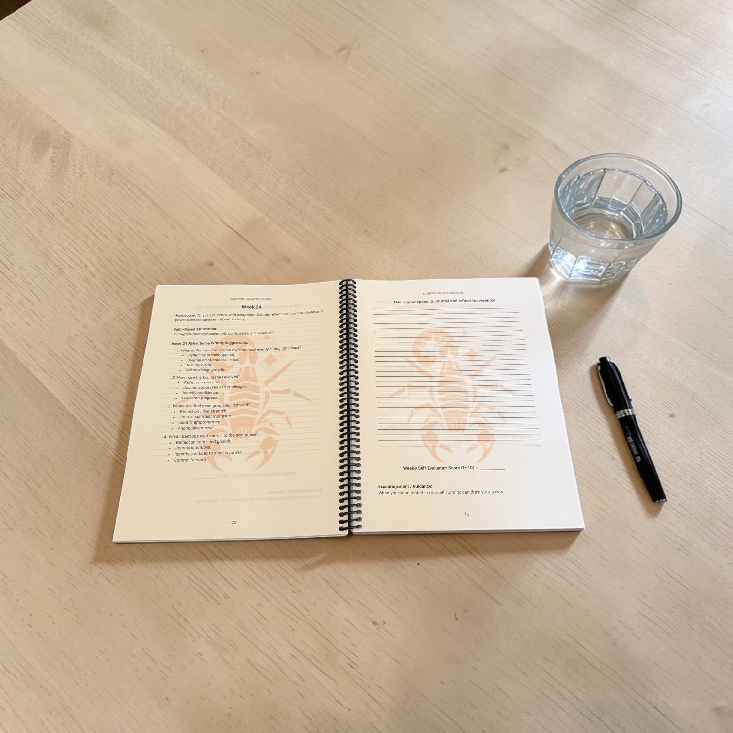 Scorpio 52-Week Zodiac Journal on a table with a pen and a glass of water.