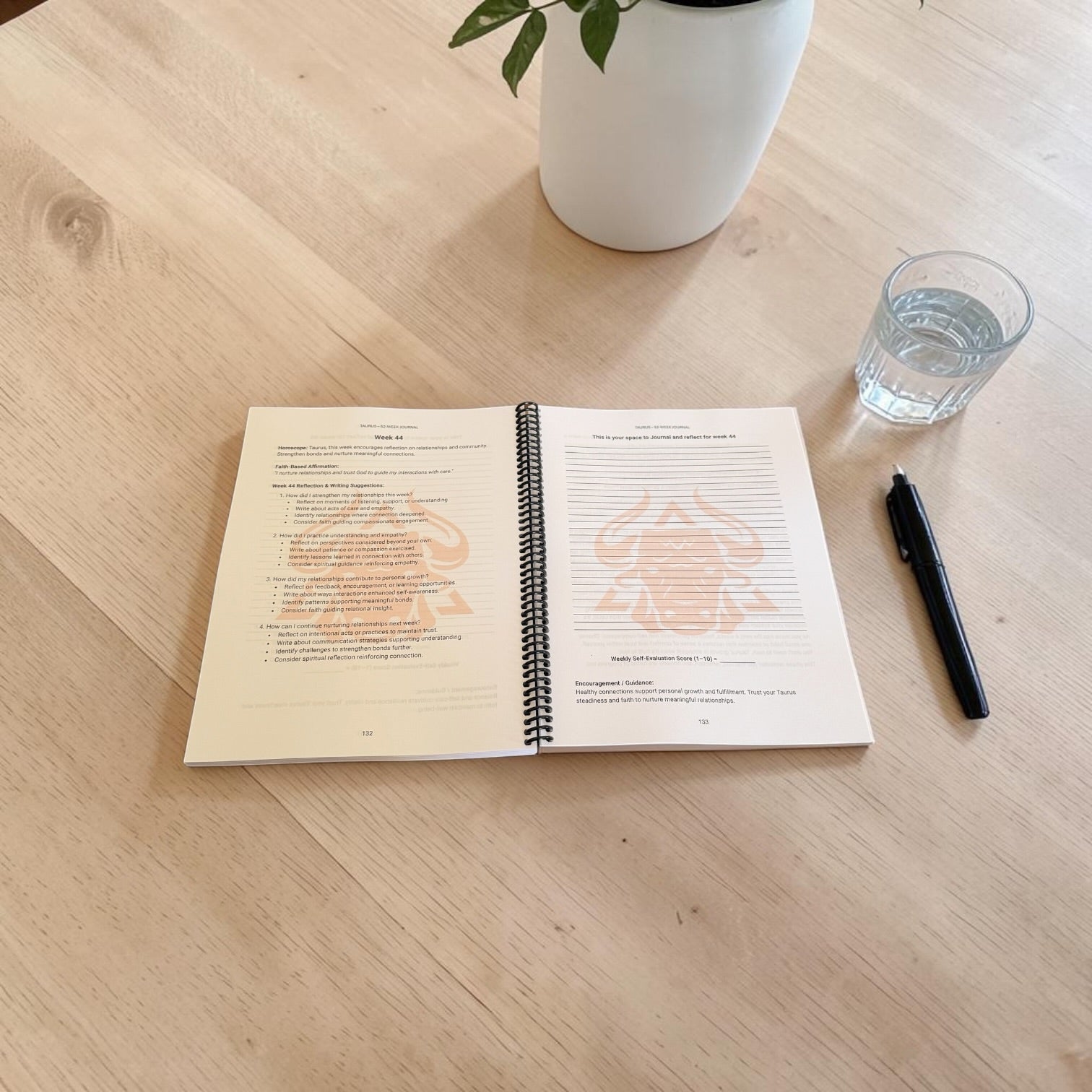 Taurus 52-Week Zodiac Journal interior lay-flat open journal image on a table with a pen, a glass of water and a plant on the table