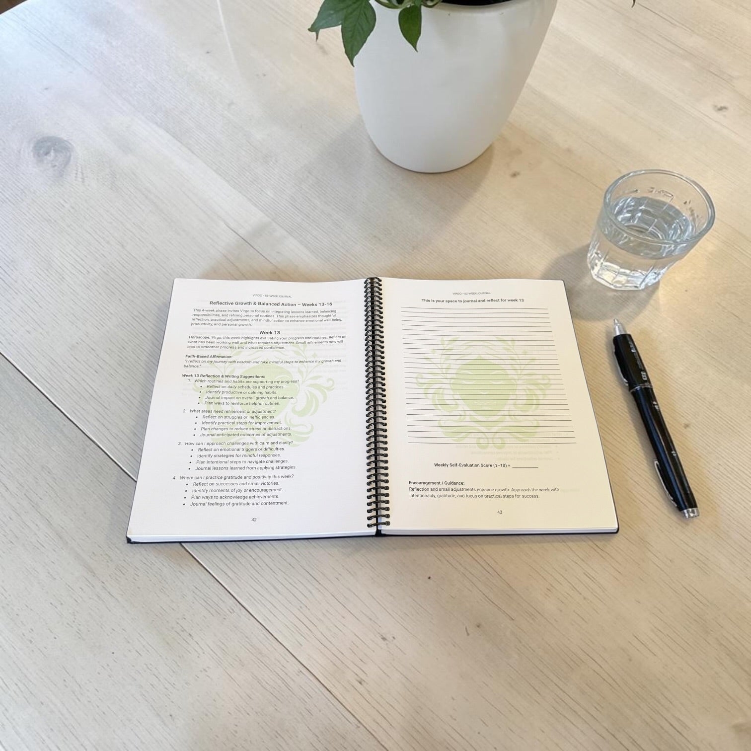 Virgo 52-Week Zodiac Journal interior lay-flat image on a wooden table with a pen and glass of water.